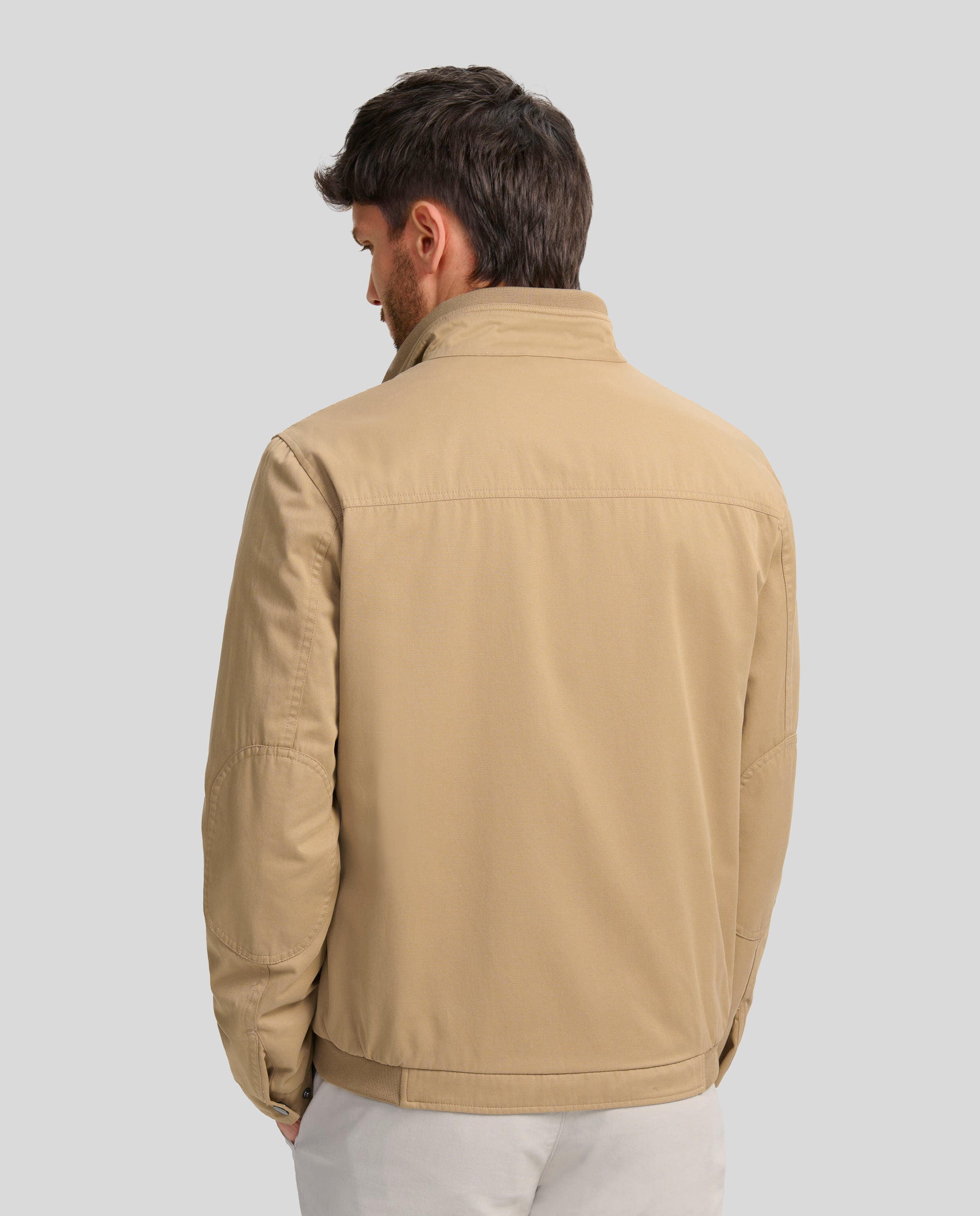 Buccino | JULIO | TOSTADO | foto de espalda |Cazadora en tejido algodón con coderas, lleva una tira de punto fino en cintura y cuello. Forrada liso a contraste. Dos bolsillos laterales de fácil acceso con broche personalizado y dos bolsillos con cremallera en el interior. Puños ajustables con broche personalizado. Cierre frontal con cremallera vista personalizada.