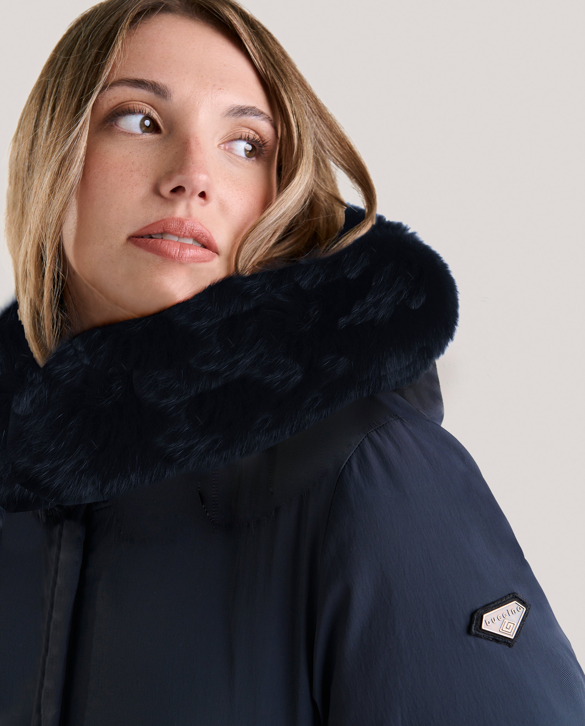 Parka lisa de pluma en tejido técnico mate.

Capucha fija con pelo natural de zorro tintado al tono y cinta Buccino.

Forrada en tejido acolchado personalizado con letras a contraste, con cordón elástico fino ajustable en cintura.

Dos bolsillos laterales de fácil acceso.

Cierre frontal con cremallera personalizada con tapeta.

Largo de prenda; 84 cm.