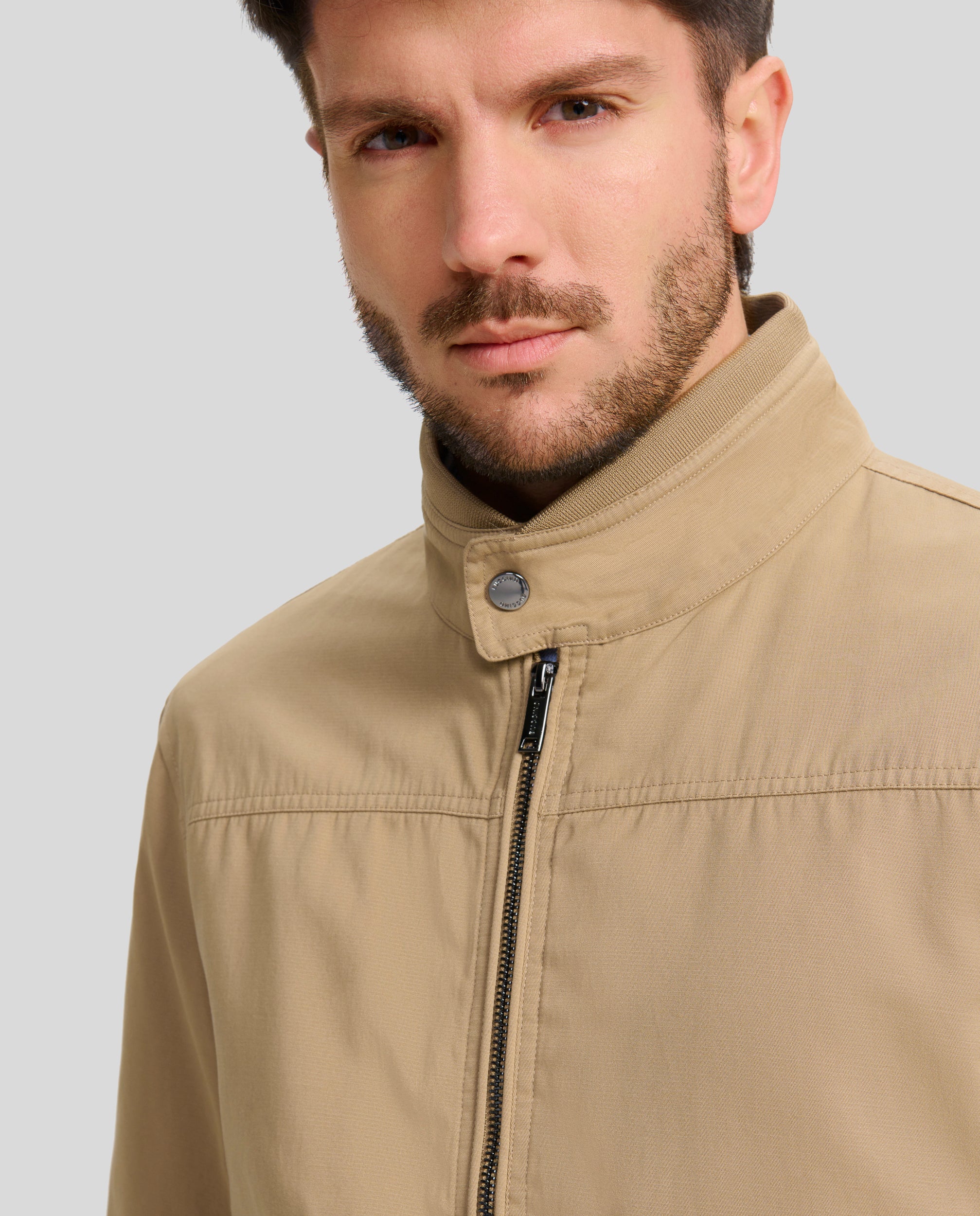 Buccino | JULIO | TOSTADO | foto de Delantero |Cazadora en tejido algodón con coderas, lleva una tira de punto fino en cintura y cuello.  Forrada liso a contraste.  Dos bolsillos laterales de fácil acceso con broche personalizado y dos bolsillos con cremallera en el interior. Puños ajustables con broche personalizado.  Cierre frontal con cremallera vista personalizada.