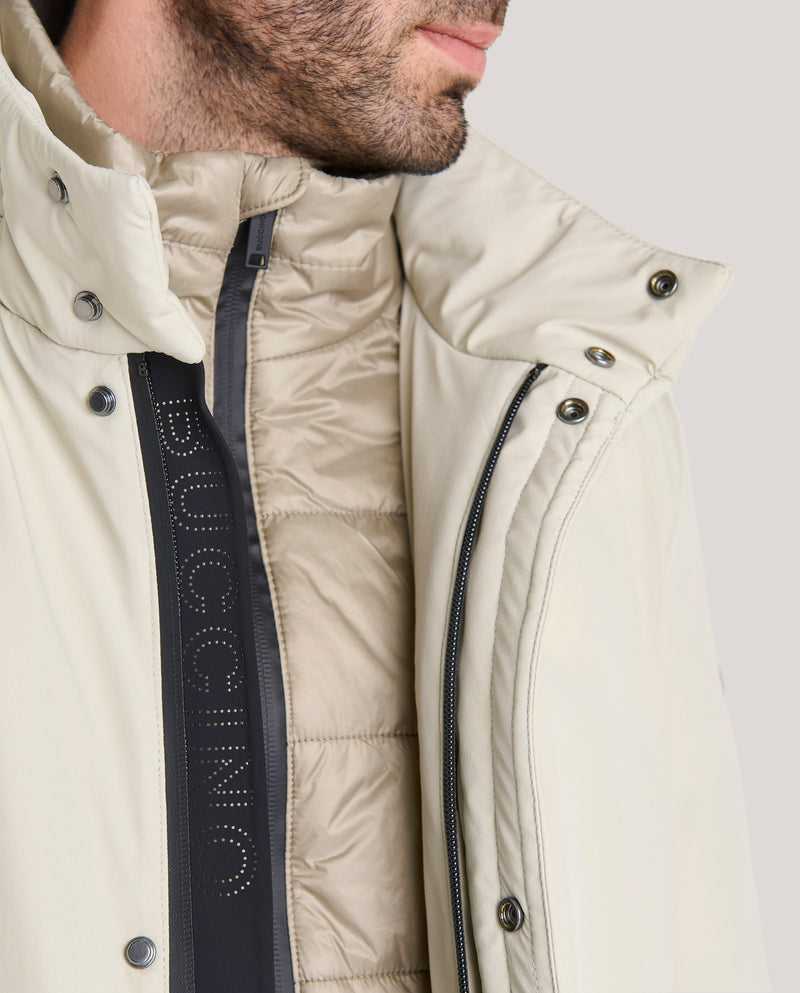 Parka lisa de largo medio en tejido liso tres capas de Cromdaltex® impermeable y transpirable con capucha oculta en el cuello con una cremallera personalizada waterproof, a efectos de chaleco lleva un pecherín desmontable en tejido técnico ligero. Dispone de abertura en el bajo espalda que cierra con broche oculto magnético y puños con punto en el interior.

Forrada en tejido técnico ligero acolchado en horizontal con relleno de boata laminada ecológica (Sorona). Dispone de dos bolsillos laterales de fácil 